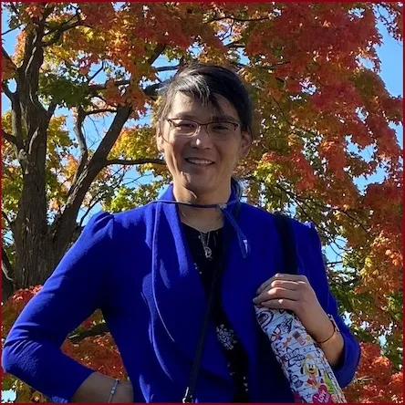 Daria Ho, blue blazer, glasses, and holding handbag
